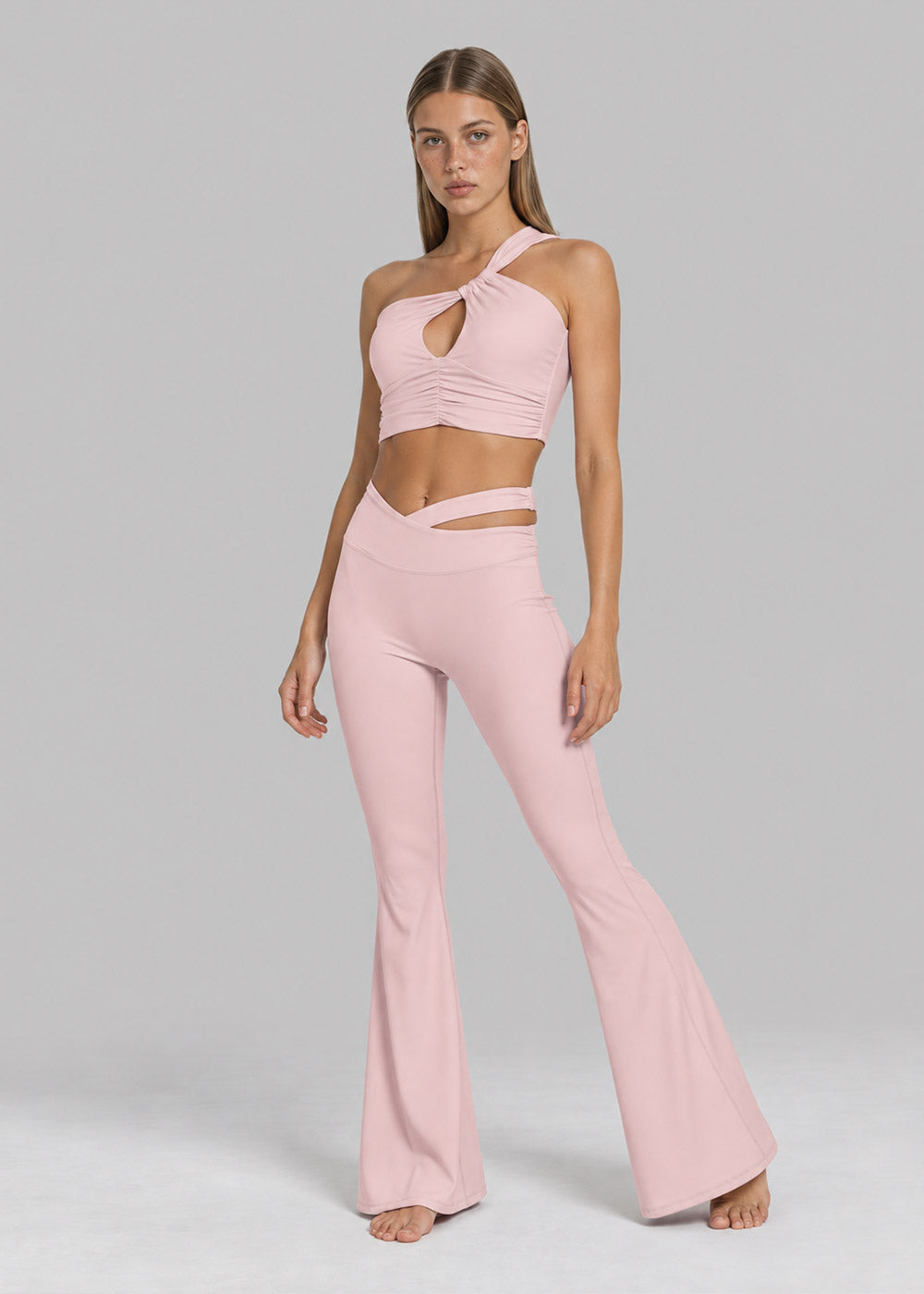 Front view of a blush pink one-shoulder cutout crop top with matching crossover-waist flare leggings