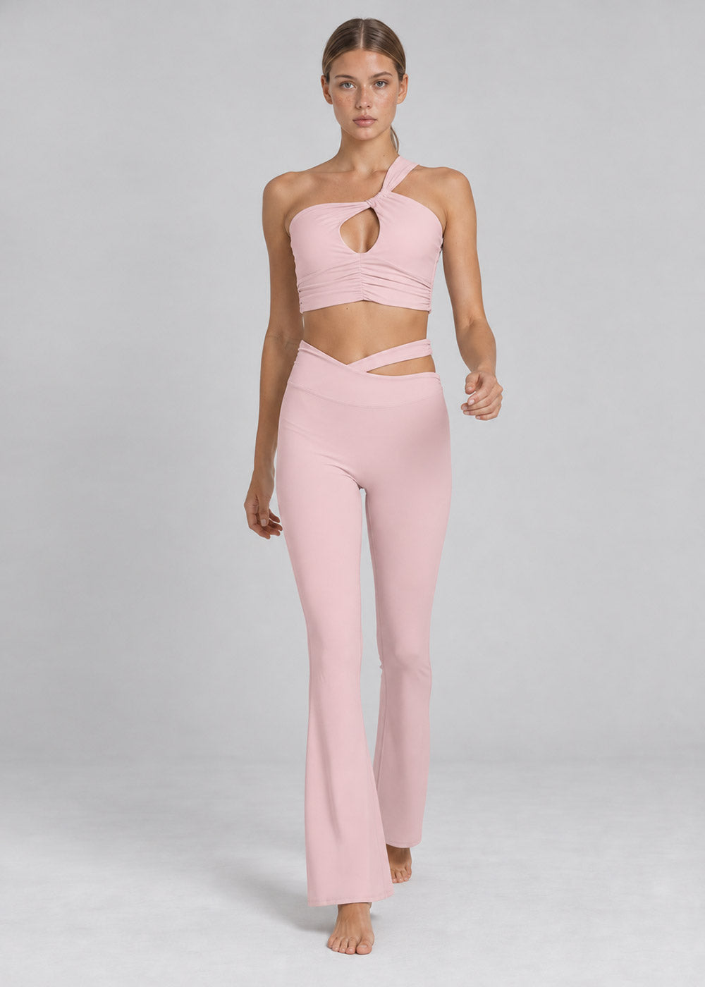 Front view of a blush pink one-shoulder cutout crop top with matching crossover-waist flare leggings