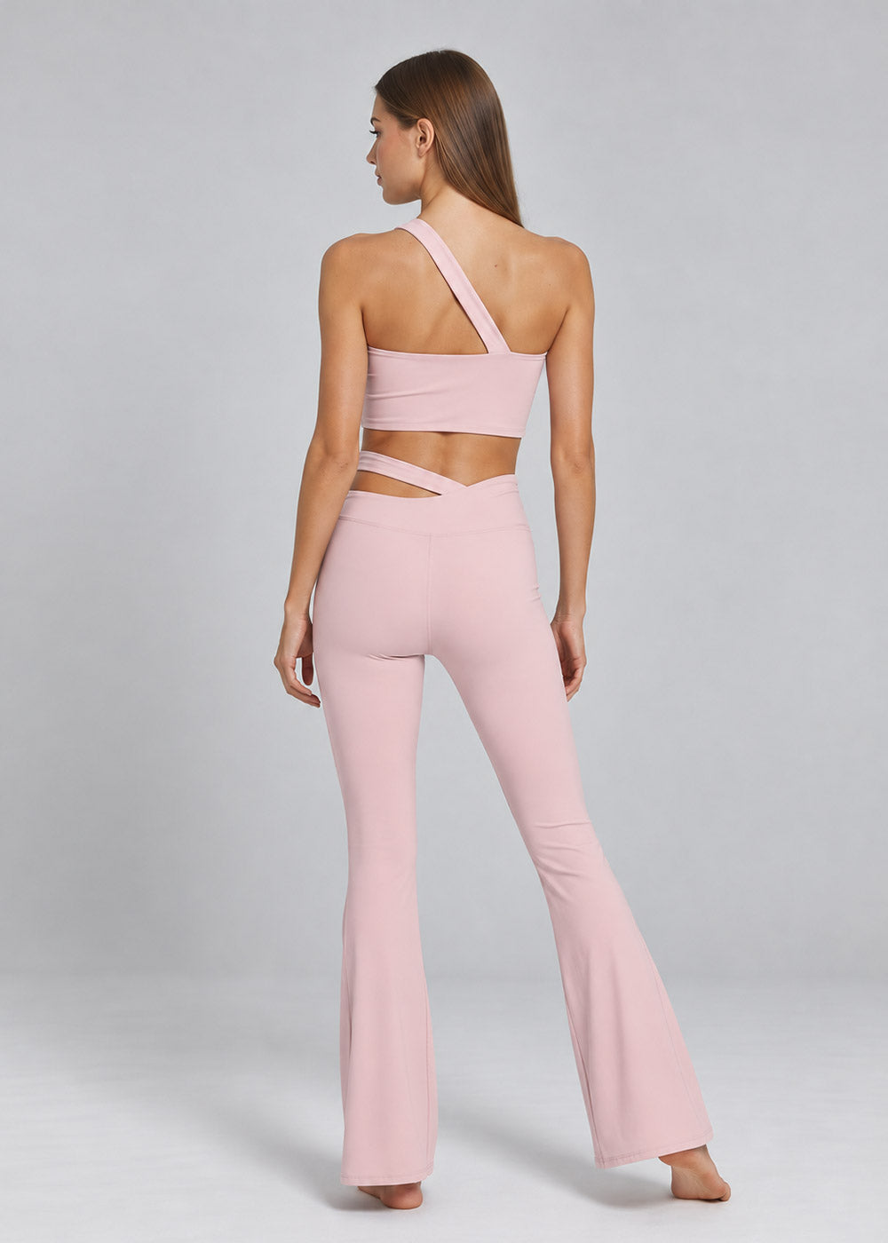 Back view of a blush pink one-shoulder crop top with crossover-waist flare leggings