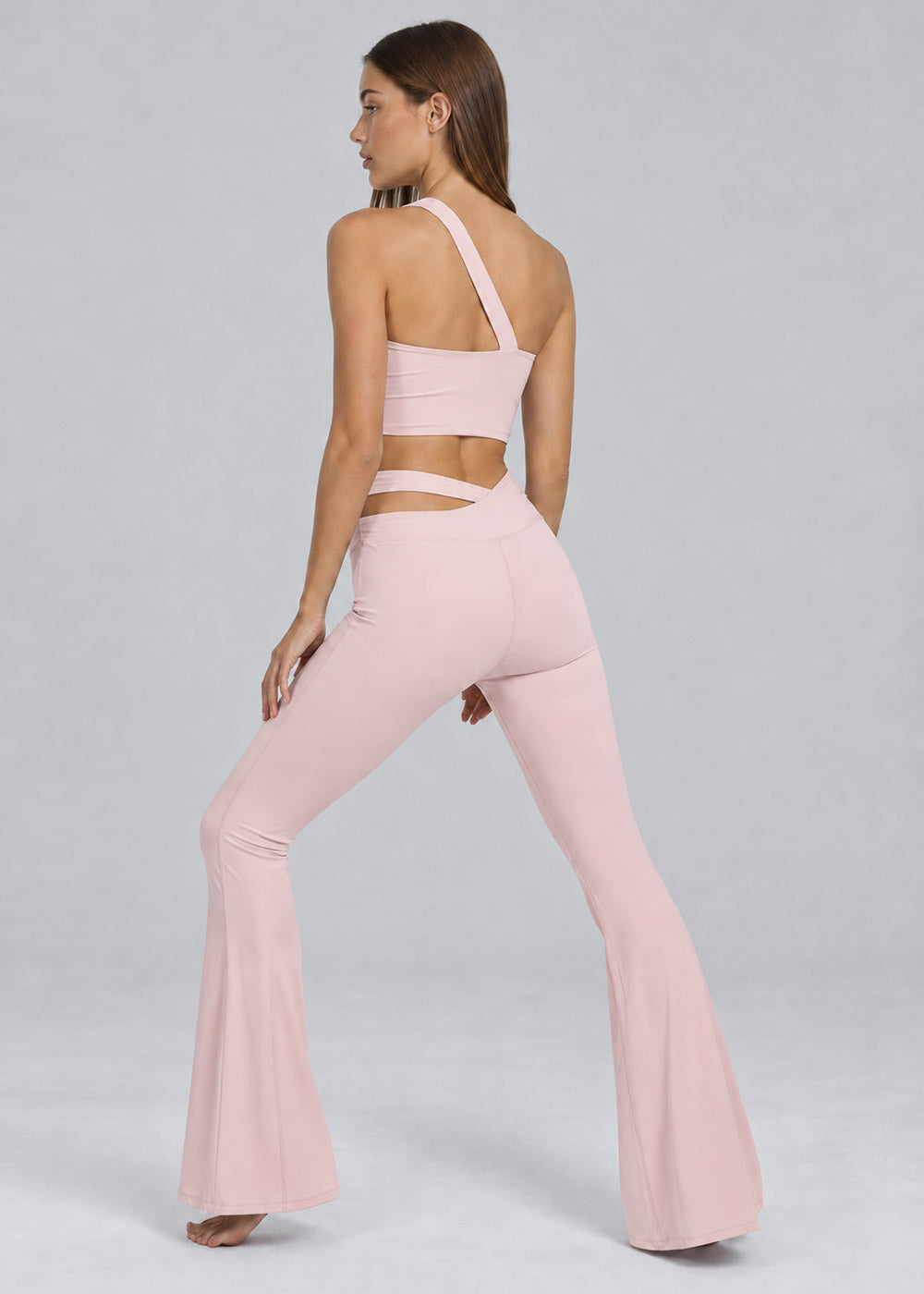 Back view of a blush pink one-shoulder crop top with matching crossover-waist flare leggings