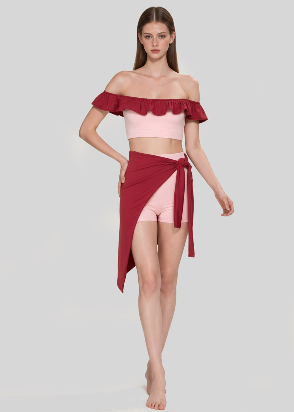 Women's blush pink off-shoulder ruffle crop top with burgundy trim, matching pink shorts and burgundy wrap skirt