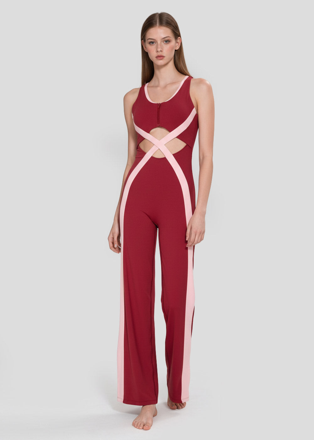 Front view of a model wearing a burgundy and blush pink colorblock wide-leg jumpsuit with waist cutouts and crossover detailing