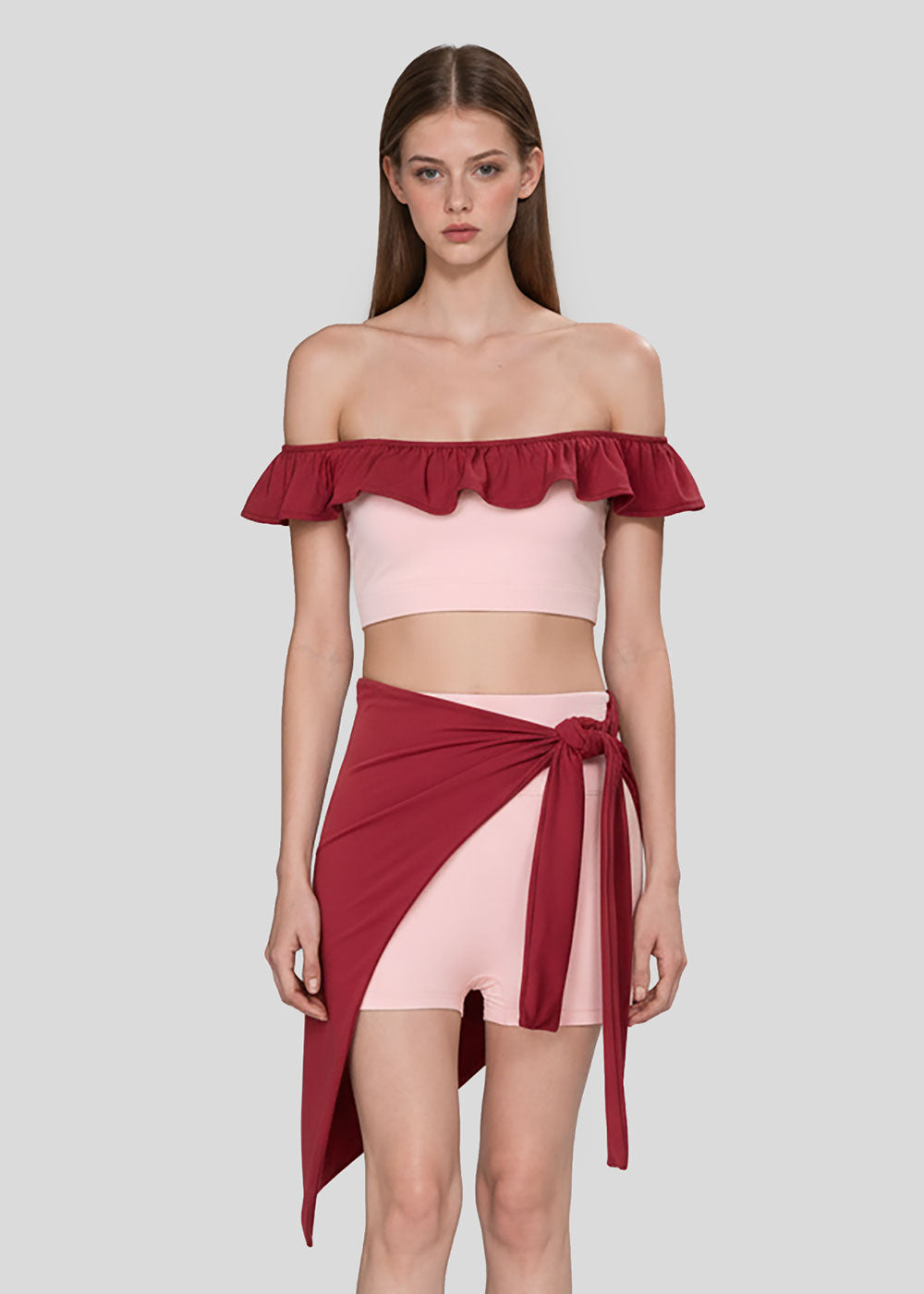 Women's blush pink off-shoulder ruffle crop top with burgundy trim, pink fitted shorts and burgundy wrap skirt