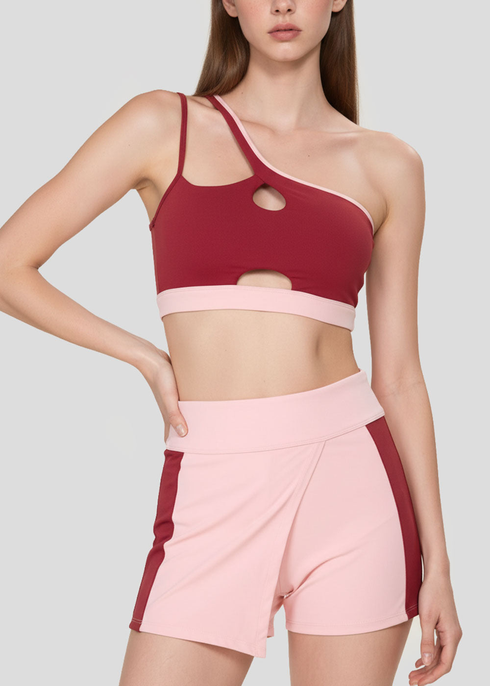 Women's burgundy asymmetrical sports bra with cutout details and blush pink high-waisted colorblock active shorts