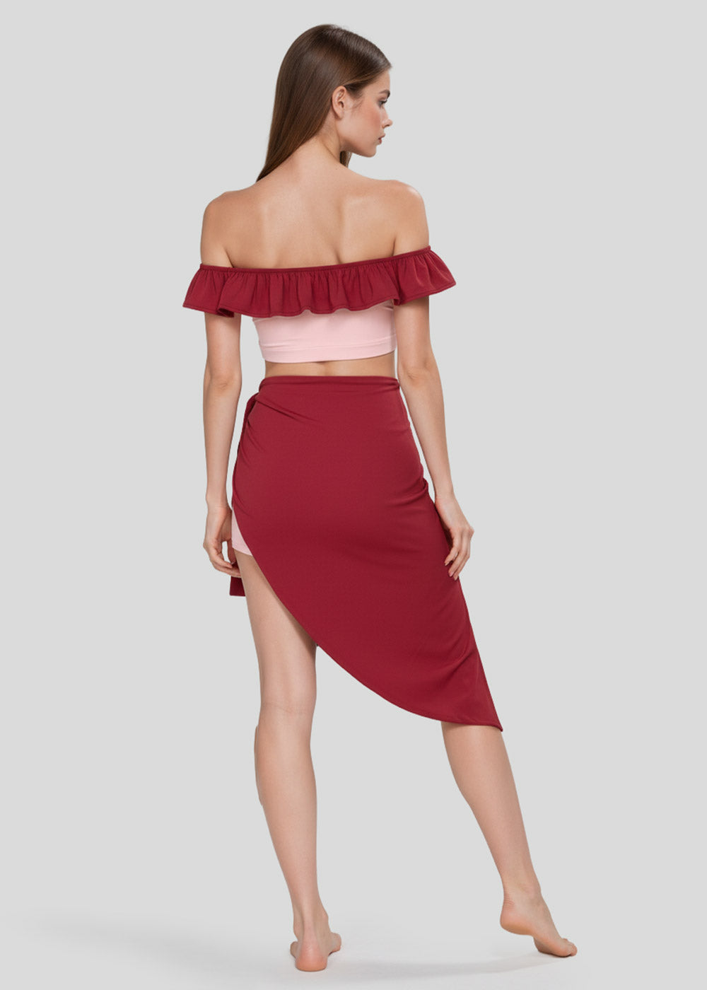 Back view of women's blush pink off-shoulder ruffle crop top with burgundy trim, matching shorts and burgundy wrap skirt