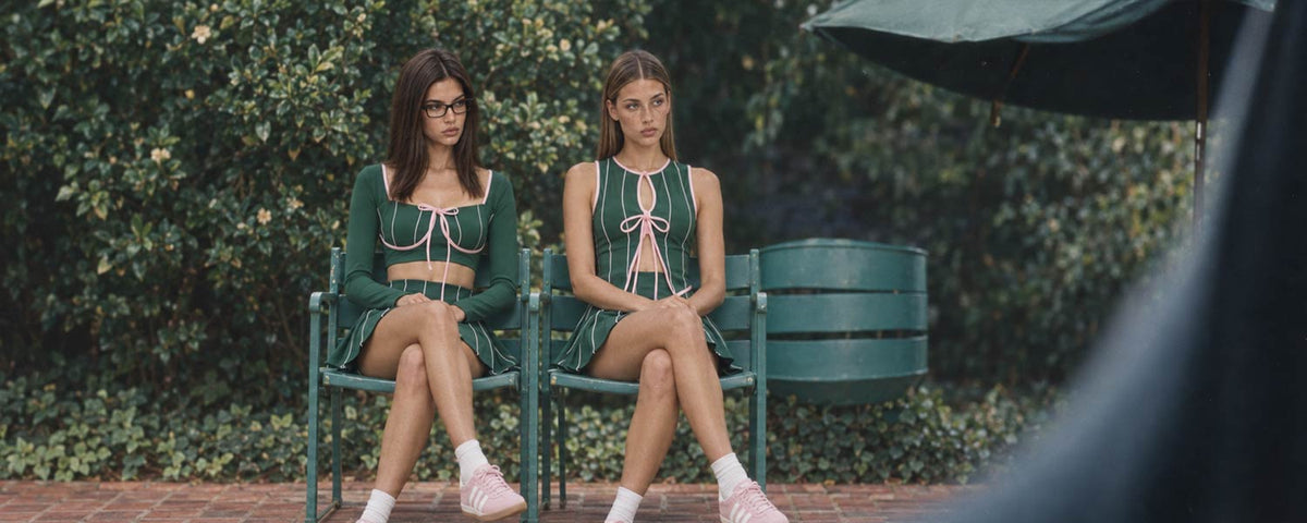 Two women wearing green and pink tennis activewear from Flowglowear, featuring feminine tops and matching tennis skirts.
