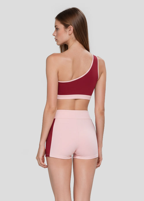 Back view of a burgundy one-shoulder sports bra with blush pink trim and high-waisted pink workout shorts with contrast side panels