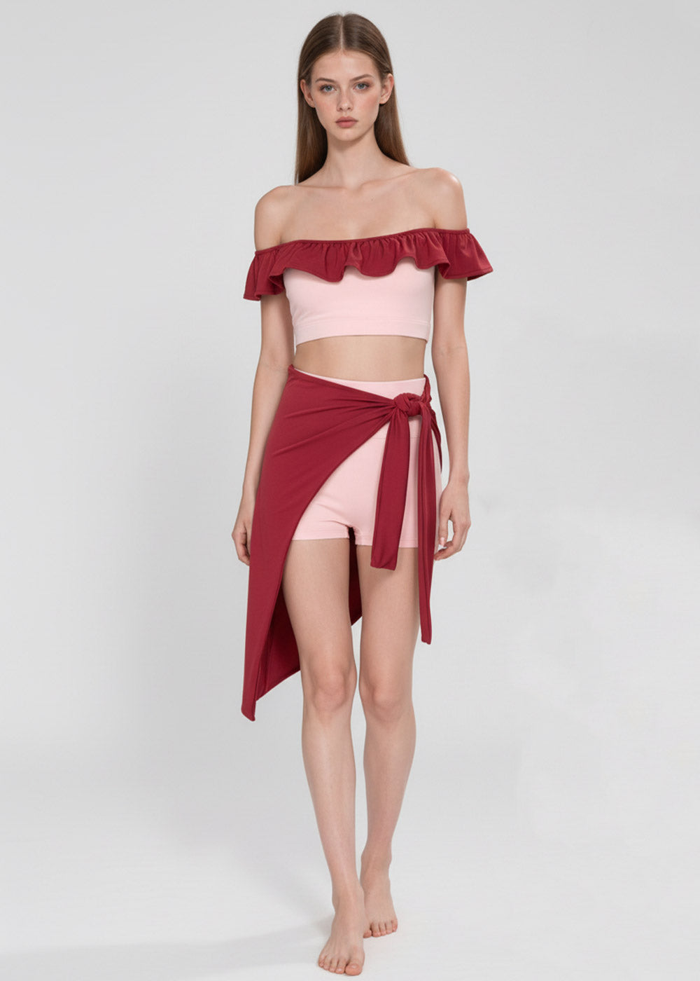 Women's blush pink off-shoulder ruffle crop top with burgundy wrap skirt and fitted shorts, front view