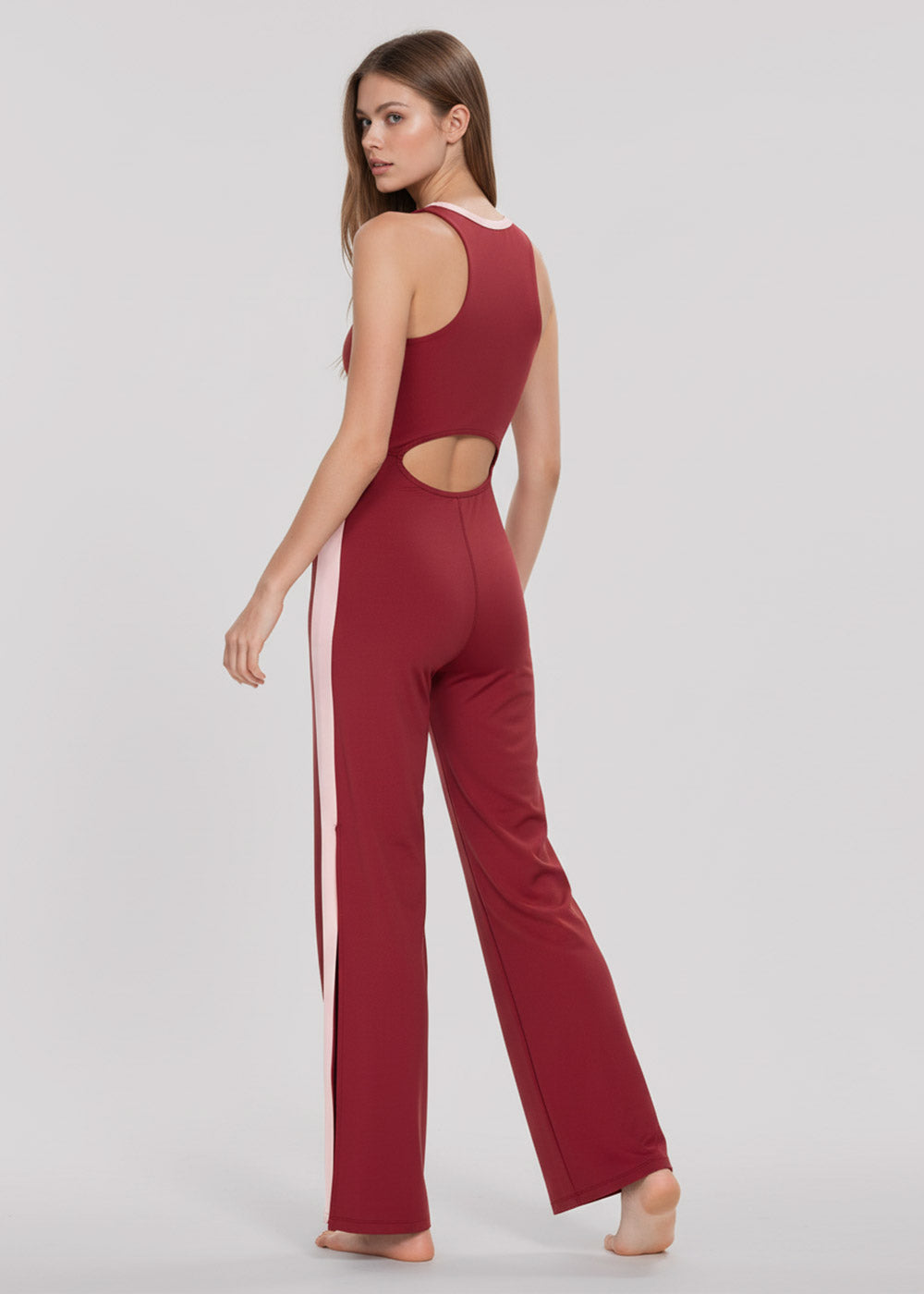 Back view of a model wearing a burgundy and blush pink colorblock wide-leg jumpsuit with an oval waist cutout and contrast side panels