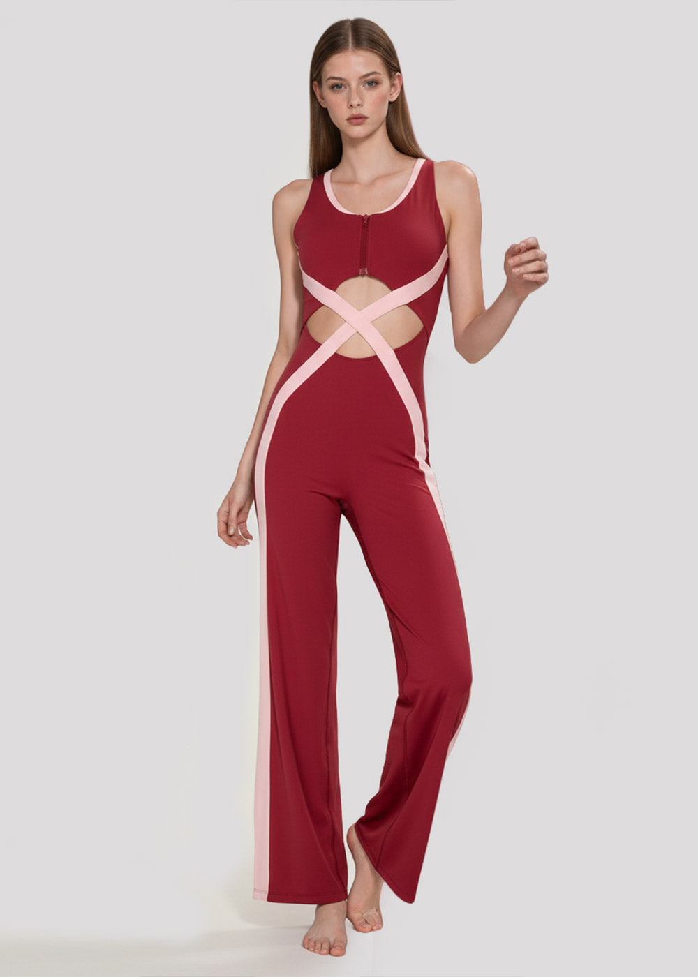 Model walking in a burgundy and blush pink colorblock wide-leg jumpsuit with waist cutouts, crossover detailing, and a front zipper
