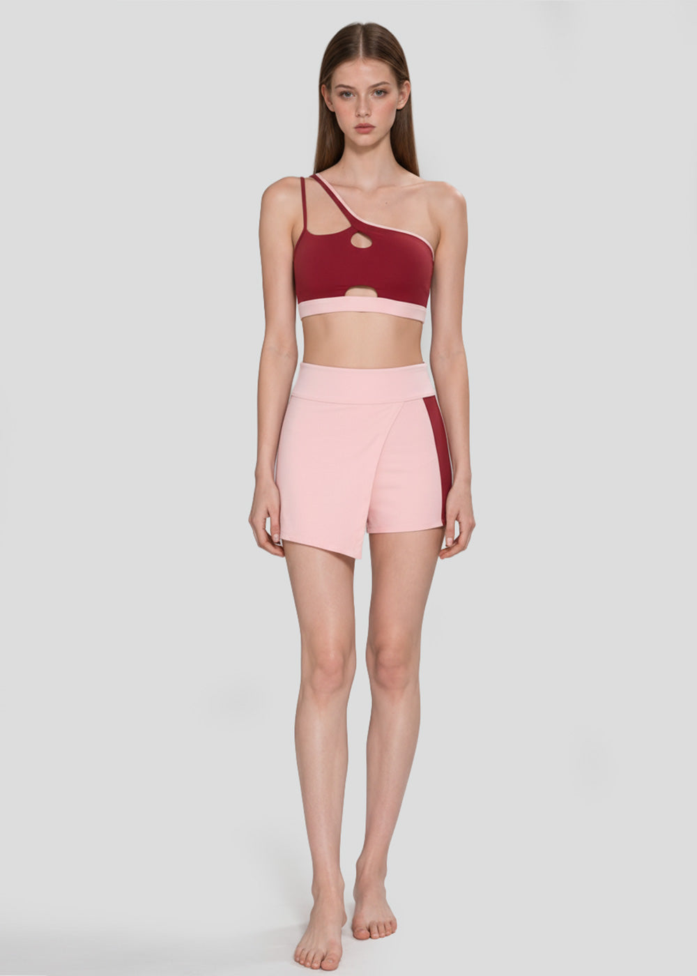 Burgundy cutout one-shoulder sports bra and blush pink high-waisted workout shorts for women, front view