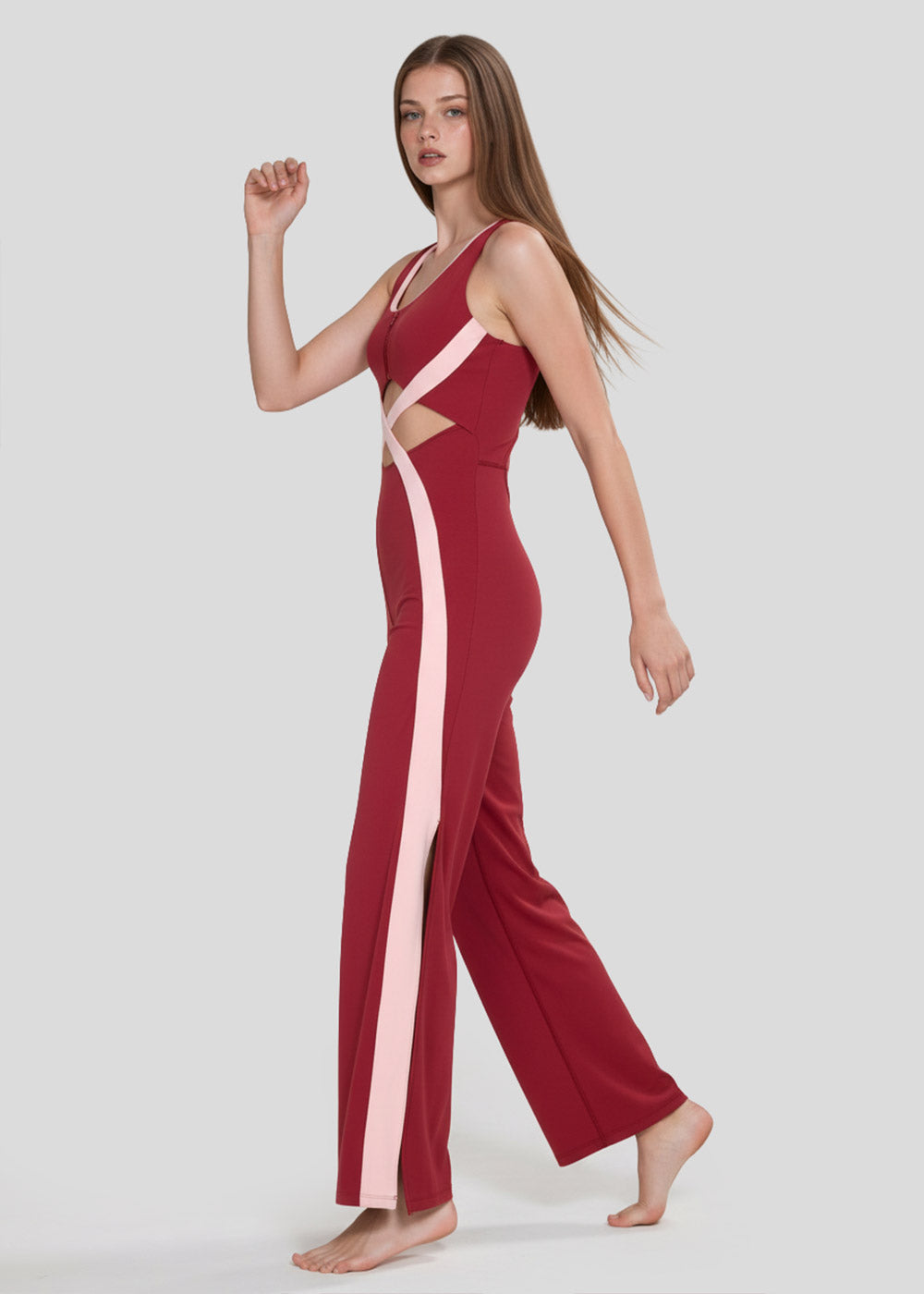 Side view of a model walking in a burgundy and blush pink colorblock wide-leg jumpsuit with waist cutouts and crossover detailing