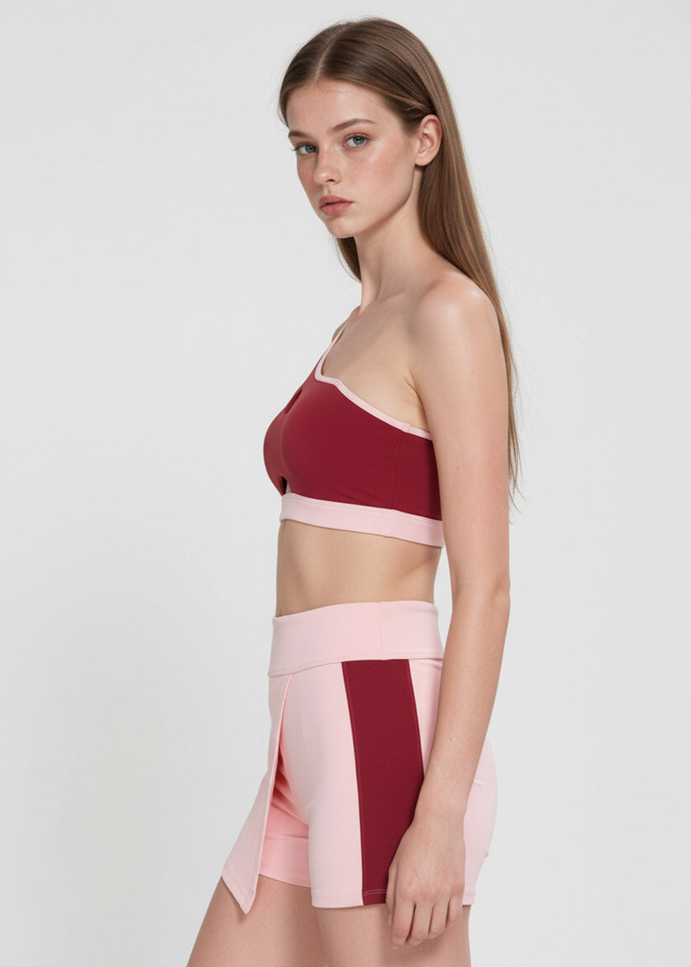 Women's burgundy one-shoulder sports bra with blush pink trim paired with high-waisted pink active shorts with burgundy side panels